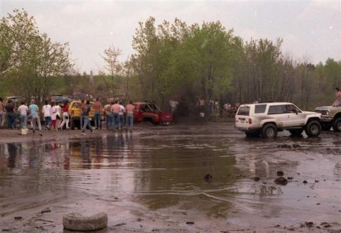 1991 Ford Bronco - A white 1989 Toyota 4Runner navigates a muddy off-road course with spectators watching.