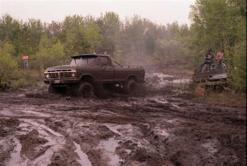 Brown 1977 Ford F-Series truck struggling in deep mud, another vehicle in background