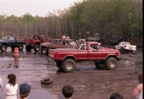 1991 Ford Bronco - Several modified pickup trucks are seen participating in an off-road event in a muddy area.