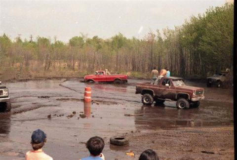1991 Ford Bronco - Multiple trucks are stuck in a mud bog while spectators watch the off-road event.