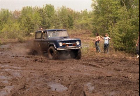 1991 Ford Bronco - This classic Ford Bronco is navigating a challenging muddy terrain, kicking up dirt as it goes.
