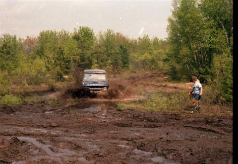 1991 Ford Bronco - An off-road vehicle navigates a challenging muddy terrain with trees in the background.