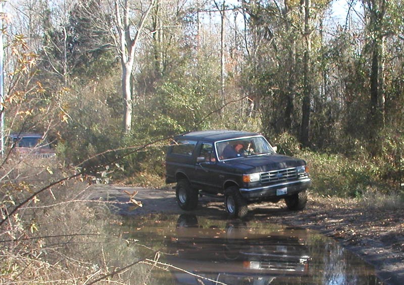 Black SUV with lifted suspension driving through a muddy puddle, front grille visible
