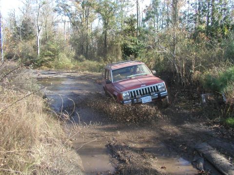 1988 Ford Bronco - This Jeep Cherokee XJ is navigating a muddy off-road trail with water obstacles.