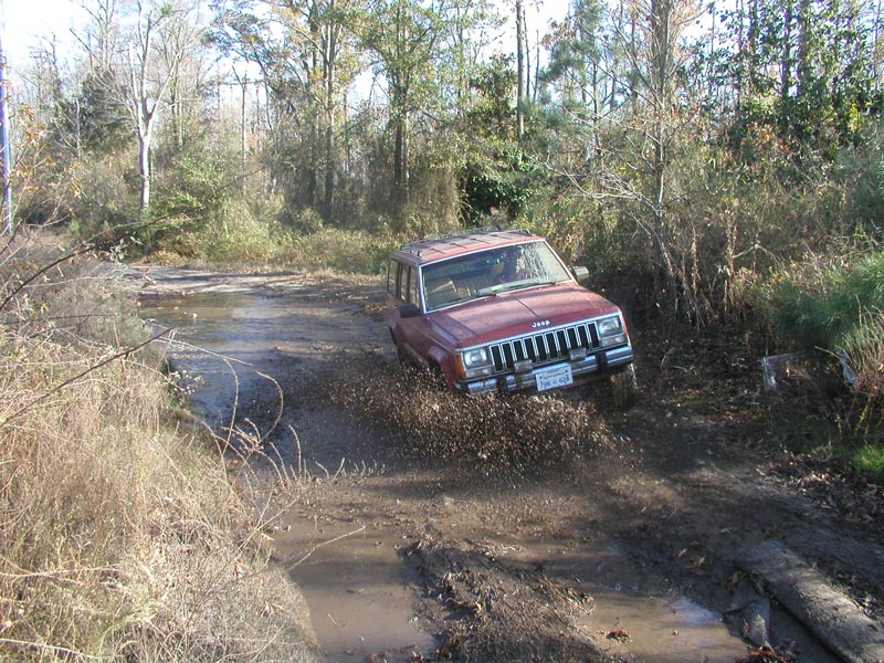 Red Jeep Cherokee XJ driving through mud and water