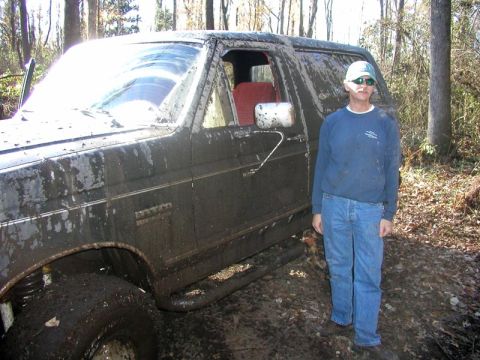 1988 Ford Bronco - A muddy Ford Bronco is seen in a wooded area with a person standing beside it.