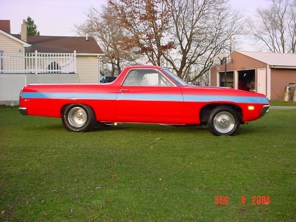 Driver-side profile of a red Ranchero with blue stripe and chrome wheels parked on grass by a house