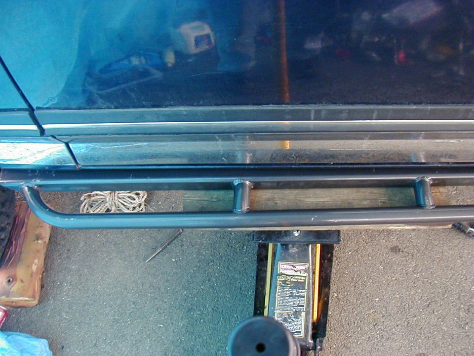 Fabricated tube rock slider held under a blue truck rocker panel by a yellow jack