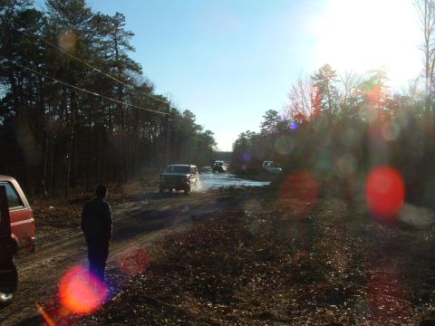 1994 Ford Bronco - Multiple SUVs navigate a muddy path through a forest on a sunny day.