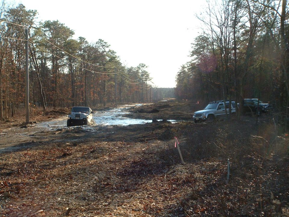 Silver Jeep Liberty and black Jeep Wrangler driving through mud and water in a wooded area