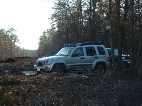 1994 Ford Bronco - Silver Jeep Liberty navigating muddy terrain with another vehicle visible in the background.