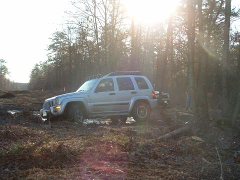 1994 Ford Bronco - A Jeep Liberty navigates a muddy, wooded trail under bright sunlight.