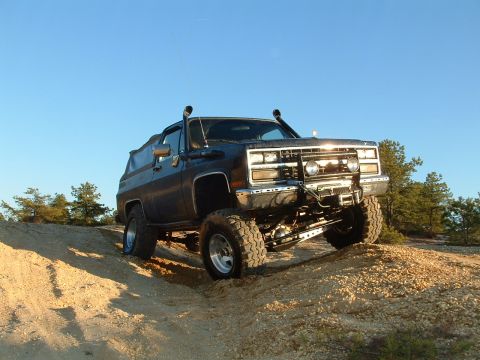 1994 Ford Bronco - This lifted SUV navigates a challenging off-road trail under a clear blue sky.