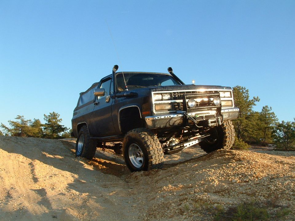 Dark SUV with snorkel and off-road tires climbing a dirt hill