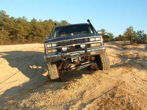1994 Ford Bronco - Off-road truck with snorkel and winch navigates sandy terrain under a clear blue sky.