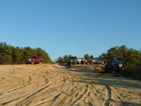 1994 Ford Bronco - Several SUVs navigate a sandy off-road course under a clear blue sky.