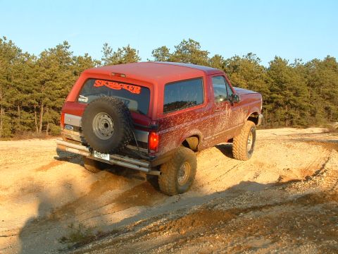 1994 Ford Bronco - Red Ford Bronco with 'SKYPACKER' sticker on rear window driving off-road.