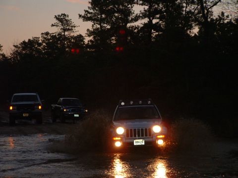 1994 Ford Bronco - Multiple SUVs navigate a water crossing as daylight fades.