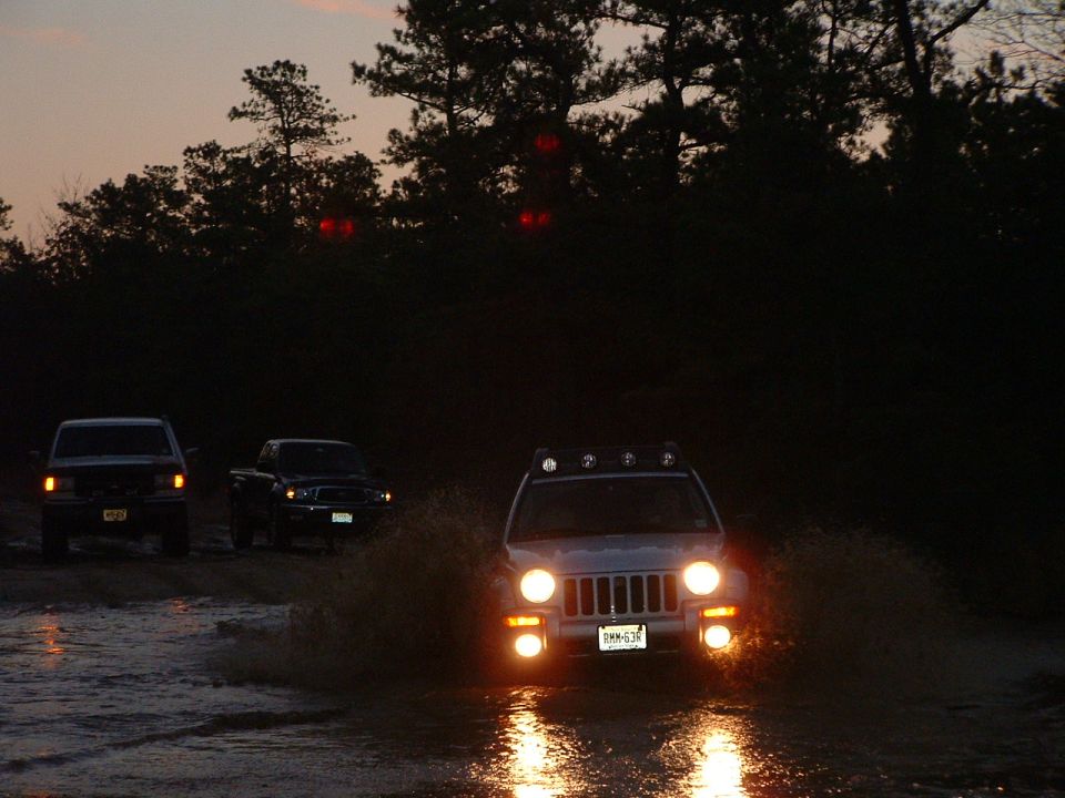 Three SUVs driving through muddy water at dusk, headlights on