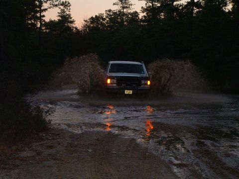 1994 Ford Bronco - A white Ford Bronco navigates a muddy path, creating dramatic water spray.