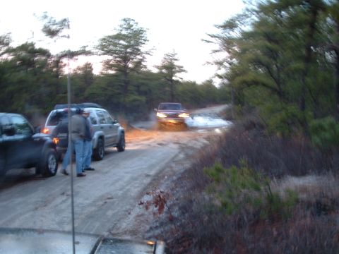 1994 Ford Bronco - Several SUVs navigate a muddy, wooded trail during daylight hours.