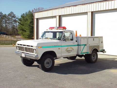 1973 Ford F-250 - This 1973 Ford F-250 truck is equipped with a utility bed and emergency lights, seen parked outside a building.