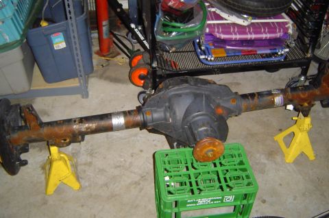 1993 Ford Bronco - A rusty rear axle assembly is supported by yellow jack stands in a garage setting.