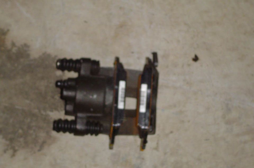 Disc brake caliper with pads and white part labels lying on a concrete floor