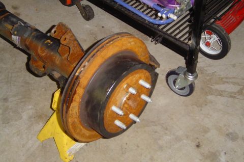 1993 Ford Bronco - A rusty rear axle assembly is supported by a yellow jack stand in a garage setting.