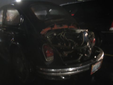 1981 Ford Bronco - Rear view of a black Volkswagen Beetle with its engine compartment open, revealing the engine and wiring.