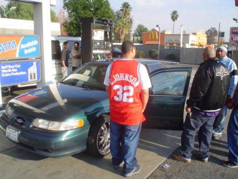 1993 Ford Taurus - A green sedan is parked at a gas station with several people standing around it.