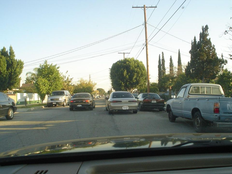 Street scene with several cars and a light blue pickup truck parked on the right