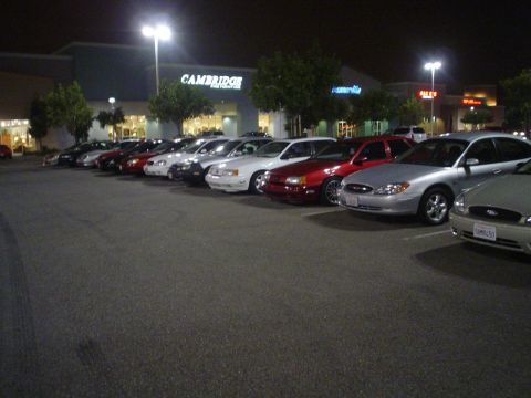 1993 Ford Taurus - A line of cars, including a silver Ford Taurus, are parked in a lot outside a Cambridge store at night.