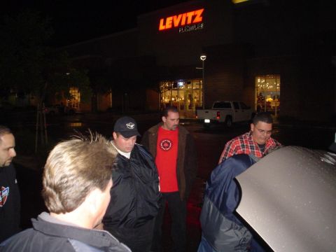 1993 Ford Taurus - A group of men inspect a vehicle's engine bay at night in front of a Levitz Furniture store.