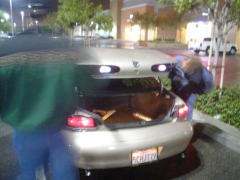 1993 Ford Taurus - A person is loading items into the trunk of a gold sedan at night.