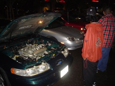 1993 Ford Taurus - The hood is open on a dark green 1993 Ford Taurus SHO, revealing its V8 engine, with other vehicles nearby.