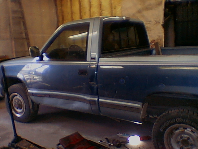 Side view of a two-tone blue regular cab pickup truck inside a garage with tools on the floor
