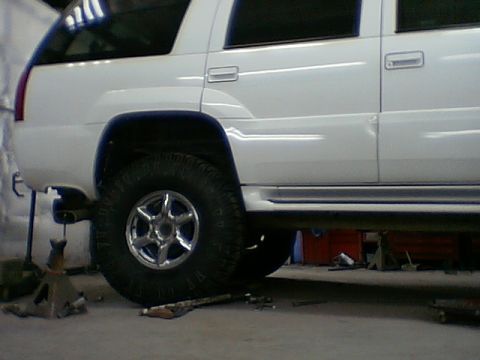 1999 Cadillac Escalade - A white 1999 Cadillac Escalade is shown from the side, with its rear wheel elevated on a jack stand for service.