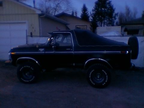 1979 Ford Bronco - Side view of a black Ford Bronco with a soft cover over the rear section and a spare tire mounted on the back.