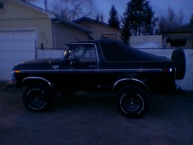 Black lifted Ford Bronco in profile at dusk with soft top and white-lettered tires