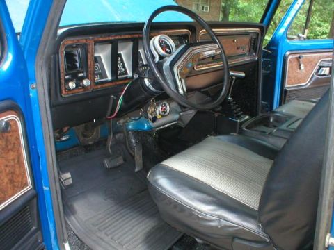 1978 Ford Bronco - Interior view from the passenger side of a blue Ford truck/SUV, showing the woodgrain-accented dashboard, two-spoke steering wheel, floor-m…