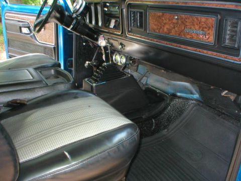 1978 Ford Bronco - Interior of a Ford Ranger XLT showing woodgrain dash trim, manual floor shifter, gray vinyl bench seat and rubber floor mats.