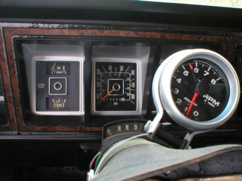 1978 Ford Bronco - Close-up of a vehicle instrument cluster with woodgrain-look trim, showing a fuel/oil/temp gauge pod, a speedometer reading in MPH, and an…