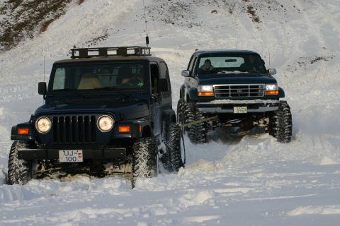 1996 Ford Bronco - Two modified 4x4s navigate a snowy terrain, with one vehicle assisting the other.