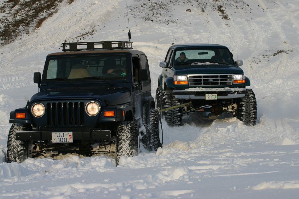 Dark green Jeep Wrangler and lifted green Ford truck in deep snow, front 3/4 view