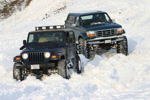 1996 Ford Bronco - Two modified 4x4s navigate a snowy terrain, one possibly requiring assistance from the other.