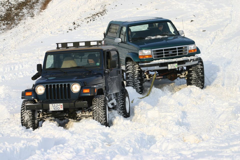 Green lifted Ford truck and dark Jeep Wrangler in deep snow off-road