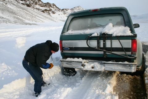 1996 Ford Bronco - A person digs a green Ford Bronco out of a snowdrift on a remote, snowy road.