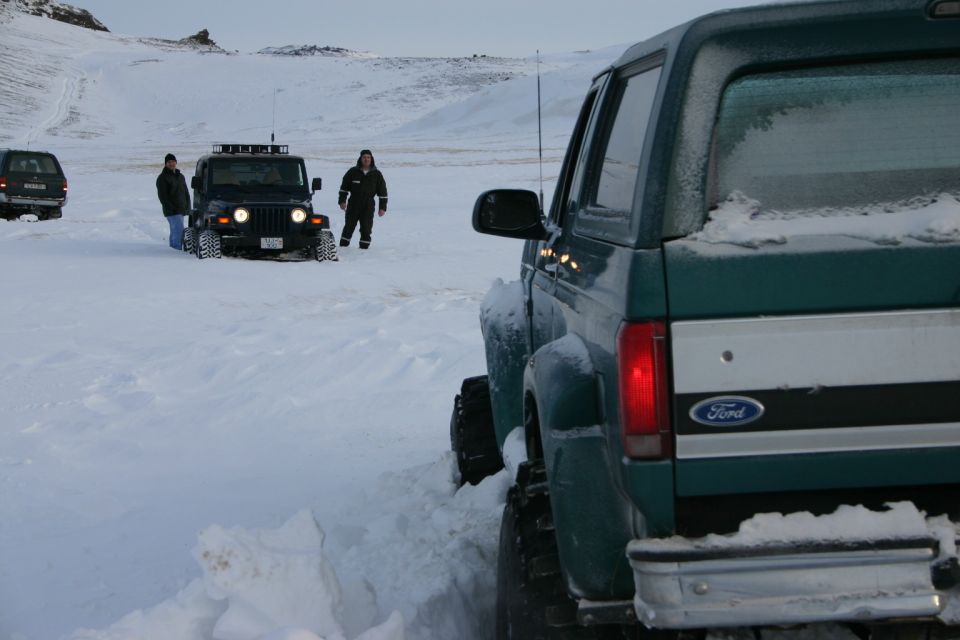 Snow-covered green Ford truck rear with a black Jeep and people in a snowy field