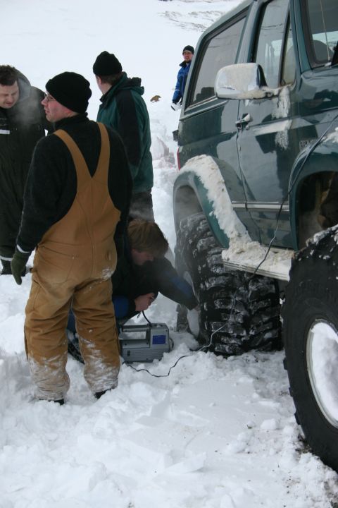 1996 Ford Bronco - People work on a 1996 Ford Bronco's tire in deep snow, possibly using a portable air compressor.